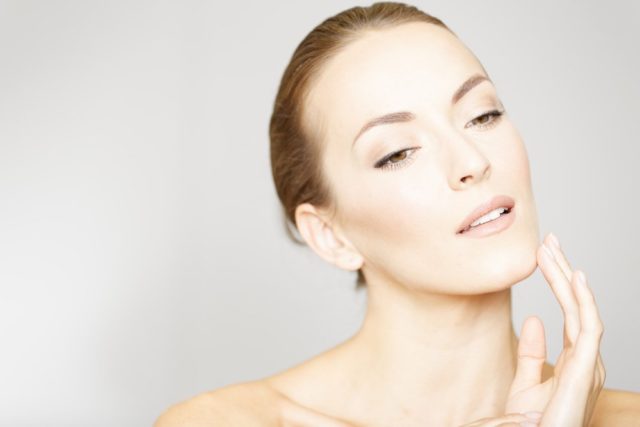 Beautiful young womans face with her hand resting on her chin and neck in a beauty style pose 1